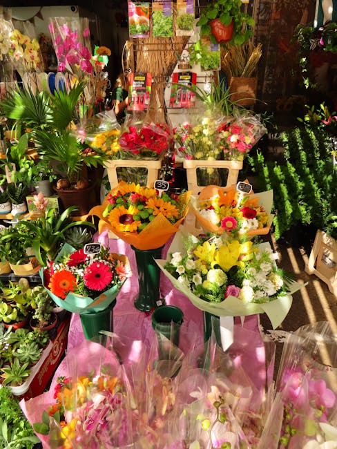 A vibrant display of fresh flower bouquets arranged on a pink table in a flower shop. The bouquets feature a variety of colorful blooms including pink gerbera daisies, yellow sunflowers, white chrysan