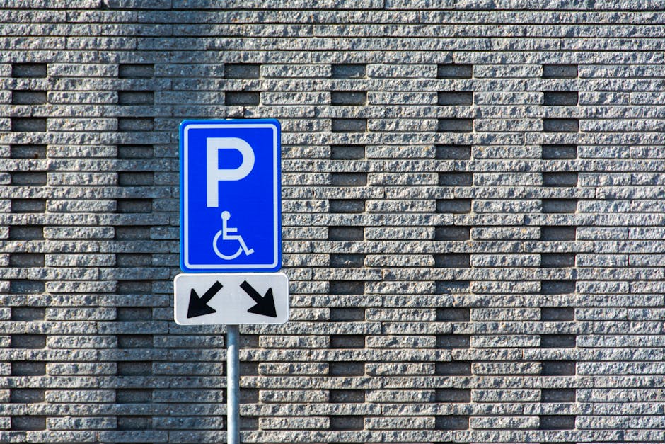 A blue parking sign with a white wheelchair symbol indicating accessible parking, mounted on a metal pole in front of a textured grey brick wall with a pattern of horizontal and vertical brick arrange
