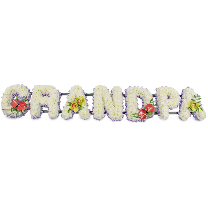 This image presents a striking funeral flower arrangement spelling out "GRANDPA" in bold, upright block capitals, flowing in a continuous line across a bright white background. Each letter is completely filled with masses of fresh white chrysanthemums, their small, layered petals overlapping so closely that no gaps are visible, creating the effect of soft, padded cushions of bloom. The overall impression is one of purity and stillness, the kind of tribute a family in South Harrow might place in a local chapel or crematorium to honour a gentle, much-loved grandparent. Along the base of every letter, a neatly folded trim of lavender ribbon is tucked just beneath the flowers, adding a cool, pastel frame that subtly lifts the design and provides definition without distracting from the simple white. Discreet dark green bars link the letters together, giving structural strength while remaining mostly hidden behind the lush flowers. Four letters are embellished with carefully placed accent sprays. On the left, the "G" carries a cluster of deep red anthuriums, their glossy, heart-shaped spathes and pale yellow spadices framed by polished green foliage, offering a poignant burst of colour. Toward the centre, the "D" repeats this theme, echoing the same red and green combination for a sense of balance. The first "A" and the final "A" are softened with sprays of yellow-green orchids, their graceful blossoms and slightly ruffled petals resting delicately among rich leaves, suggesting enduring love and precious memories. Crafted with the precision of a seasoned local florist, this tribute feels like a quiet, floral farewell that might travel from a home near Roxeth Recreation Ground to a final resting place, carrying with it the family's gratitude and respect.