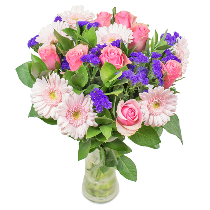 This elegant floral arrangement, crafted by skilled florists in South Harrow, features a vibrant medley of approximately seven to nine pink roses-some tightly furled, others gently blooming-showcasing their iconic spiral pattern. Intertwined with these, five to seven pale pink Gerbera daisies stand out with their large, round faces and delicate, nearly white centers, echoing the pastel palette of blossoming magnolias in Harrow's local gardens. Here and there, clusters of vivid purple statice inject a lively contrast, their papery texture adding whimsical depth like the surprising wildflowers edging Roxeth Green. Beneath, an abundance of forest-green foliage provides a lush, textured foundation, resembling the dense greenery of West Harrow Recreation Ground. The bouquet is elegantly arranged in a clear, modern glass vase, where the visible stems and sparkling water enhance the freshness and natural allure. Whether presented for a birthday, an anniversary, or as a heartfelt gift for a loved one along South Hill Avenue, this radiant collection of blooms brings an air of joyful celebration and affection, its careful composition reflecting both artistry and the welcoming character of South Harrow.